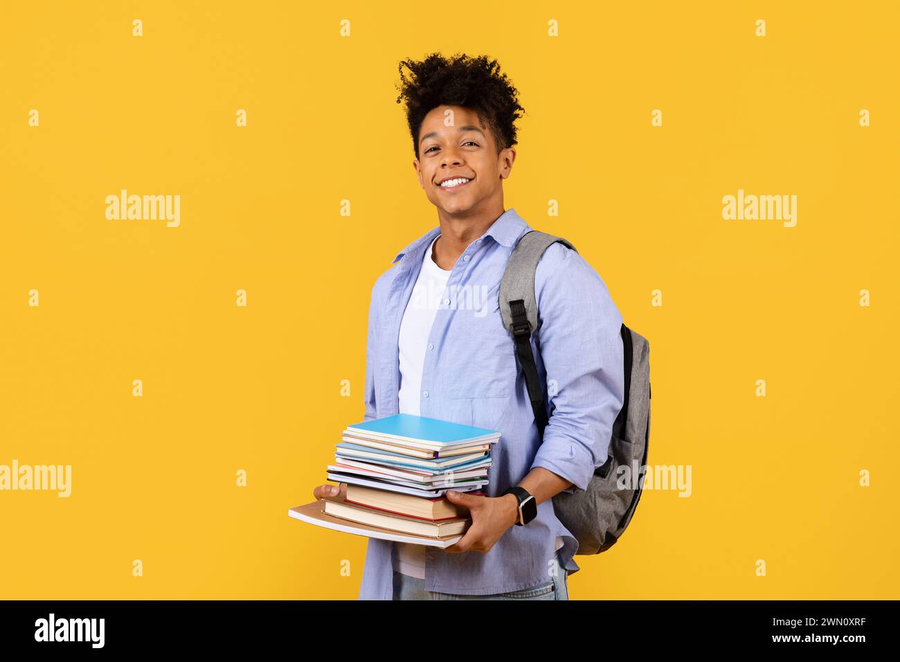 Heureux étudiant mâle noir avec sac à dos et pile de livres sur fond jaune Banque D'Images
