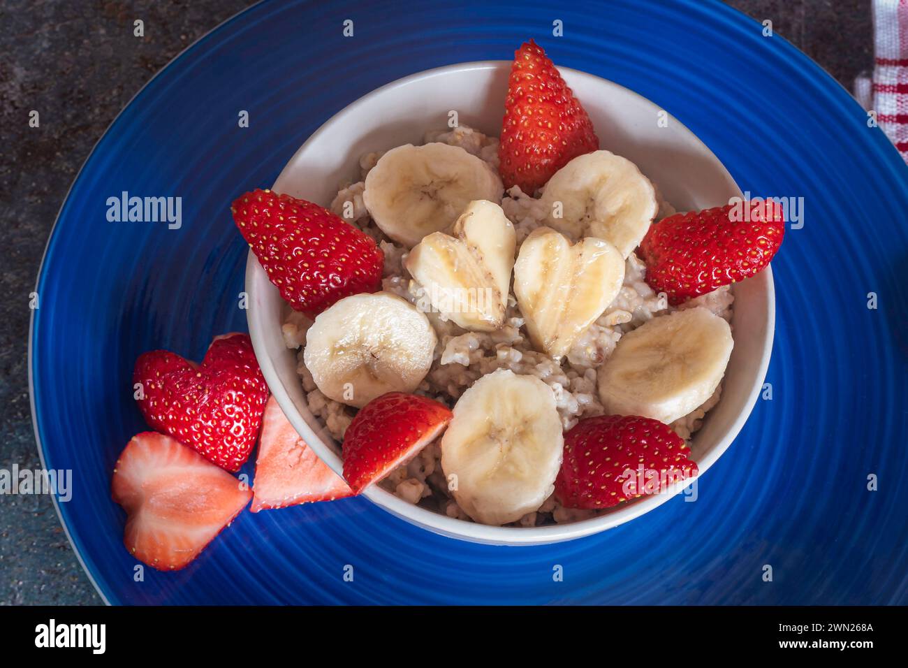 Flocons d'avoine dans un bol placé sur une assiette bleue , servi avec des fraises et des bananes coupées en forme de coeur, petit déjeuner sain, alimentation saine, Banque D'Images