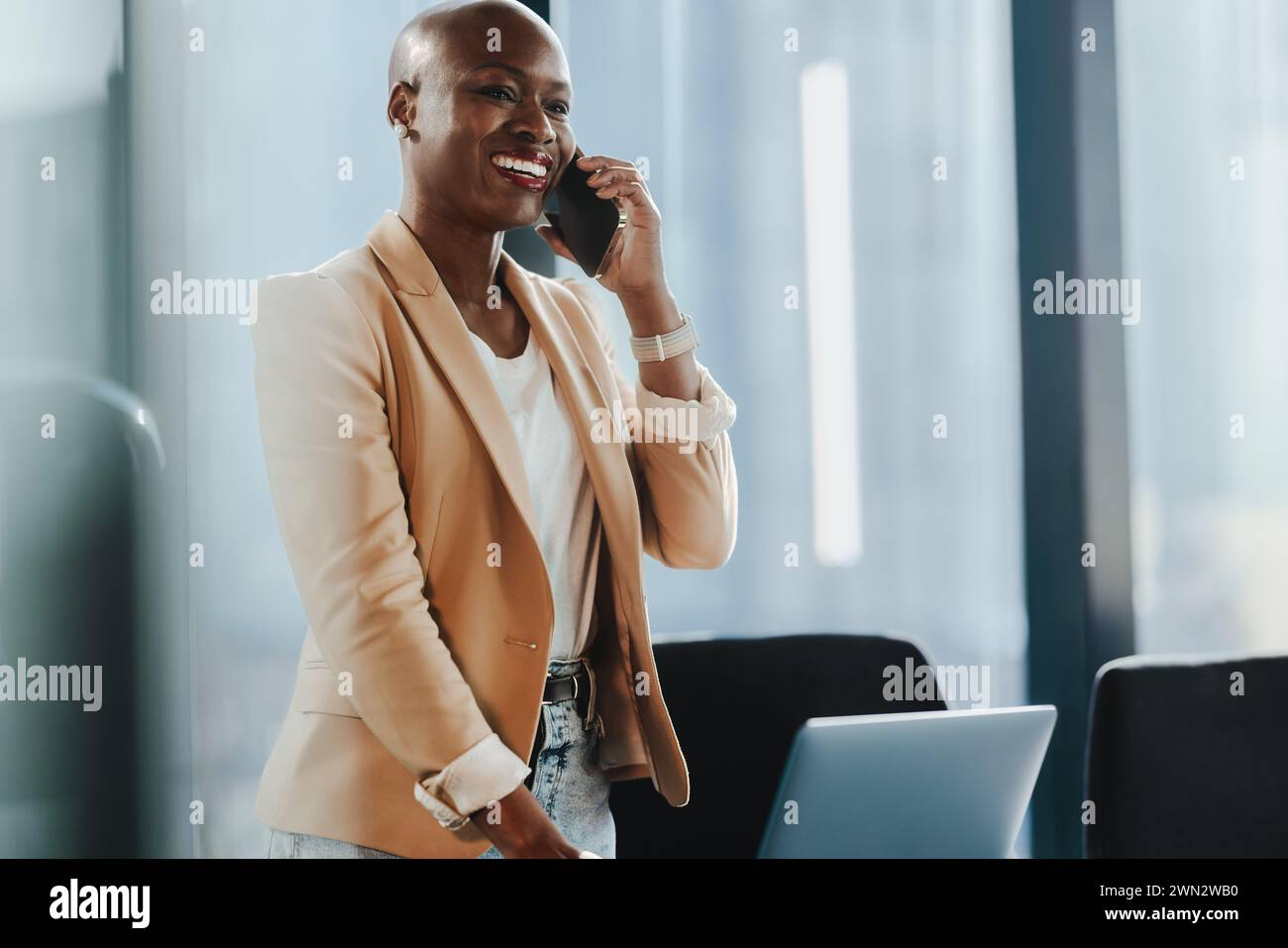 Femme d'affaires prospère debout dans son bureau, utilisant son smartphone pour la communication. Elle semble heureuse et professionnelle, discutant et parlant w Banque D'Images
