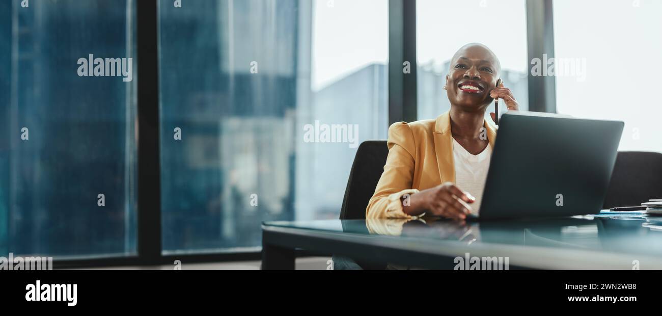 Femme d'affaires dans un bureau moderne, en utilisant son ordinateur portable et parlant au téléphone. Elle est confiante et réussie, vêtue d'une tenue d'entreprise. Comm. Femme Banque D'Images