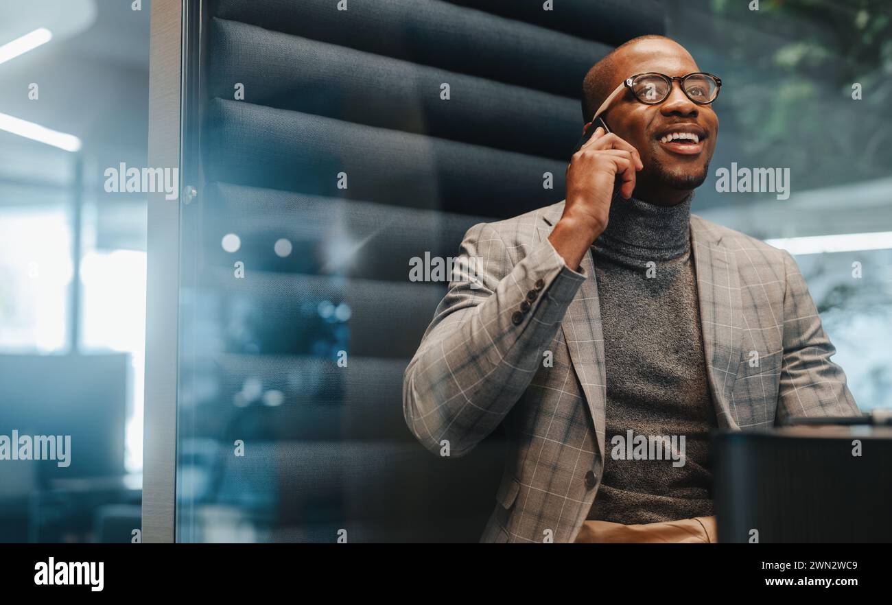 Homme d'affaires dans un espace de bureau, utilisant son smartphone pour communiquer et discuter du succès de l'entreprise. L'entrepreneur porte des lunettes et semble heureux et Banque D'Images