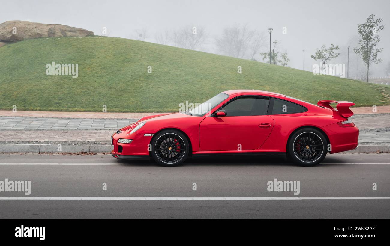 Porsche 911 rouge par un matin brumeux. Vue de profil de côté de la voiture de sport Porsche 997 près d'une colline d'herbe et d'un rocher Banque D'Images
