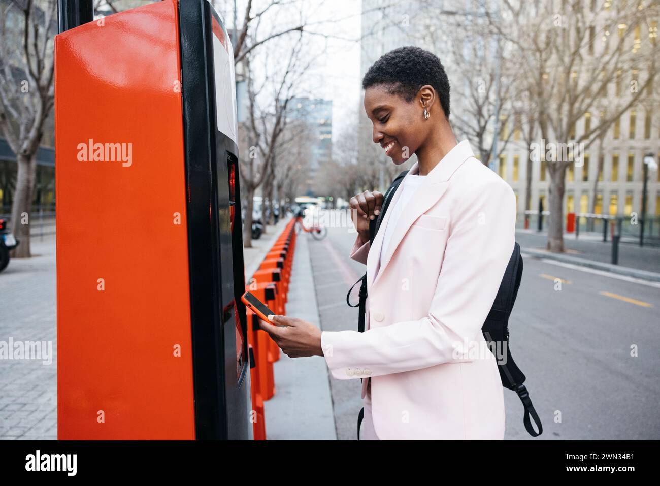 Femme d'affaires élégante utilisant son téléphone portable pour louer un vélo de ville sur son chemin de travail. Banque D'Images