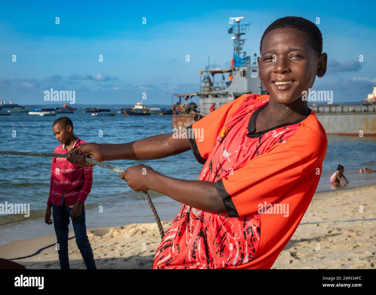 Un jeune garçon aide à transporter un bateau sur la plage de Stone Town, Zanzibar, Tanzanie. Banque D'Images