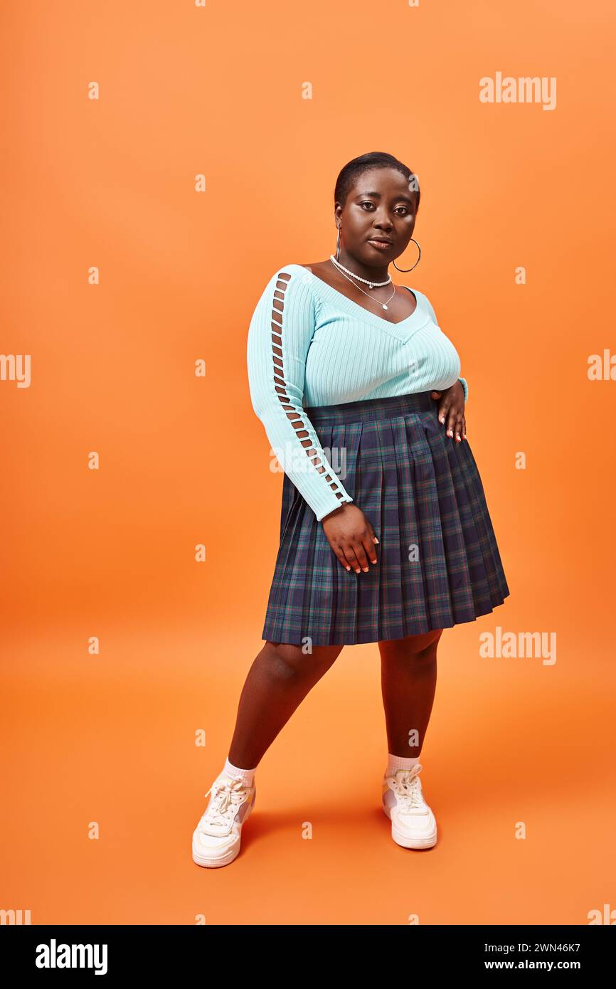Fashion-forward plus taille femme afro-américaine en jupe plaid et manches longues bleues sur orange Banque D'Images