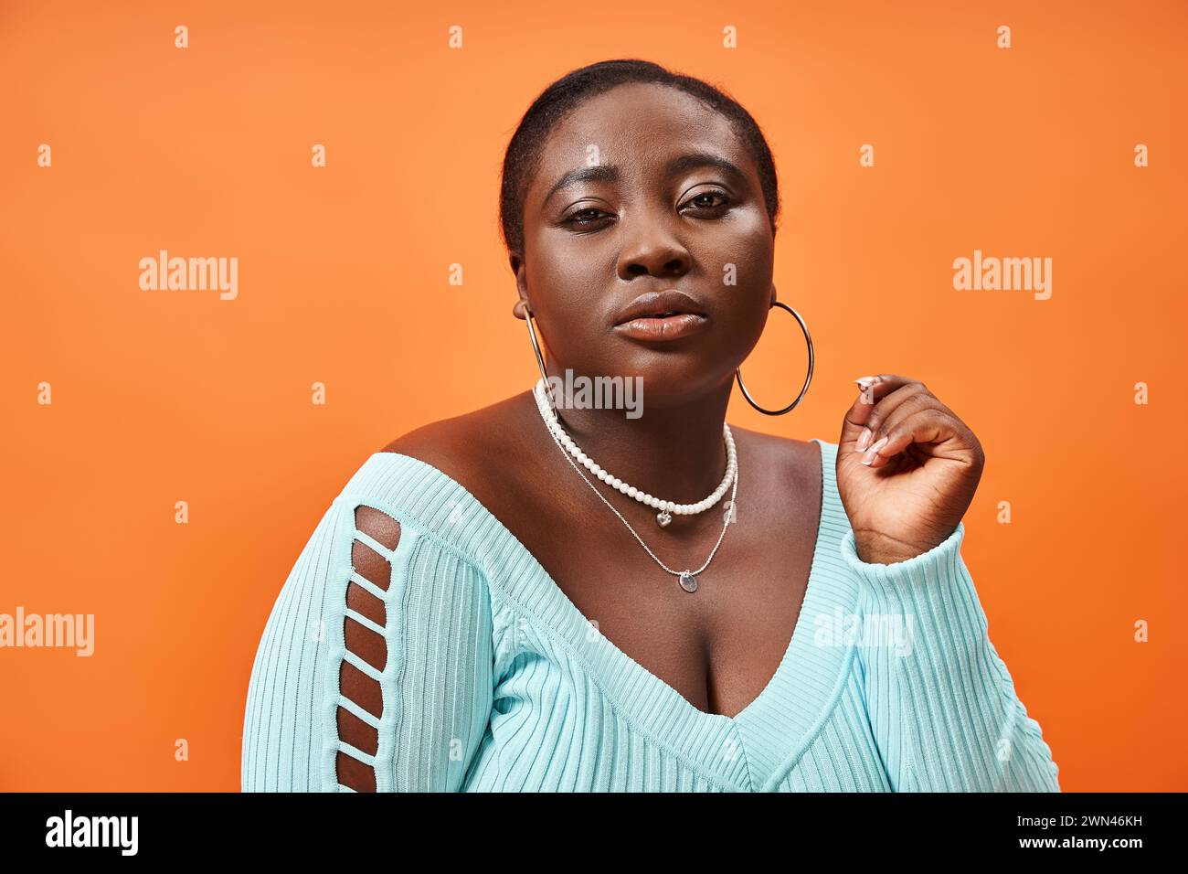 body positive afro-américaine femme en jupe à carreaux et manches longues bleues posant sur fond orange Banque D'Images