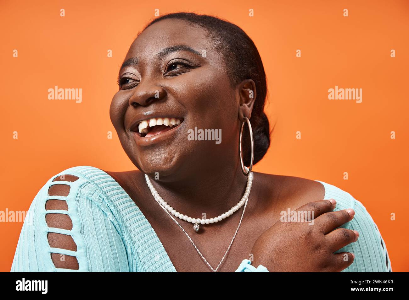 portrait de joyeuse femme afro-américaine de taille plus en manches longues bleues sur fond orange Banque D'Images