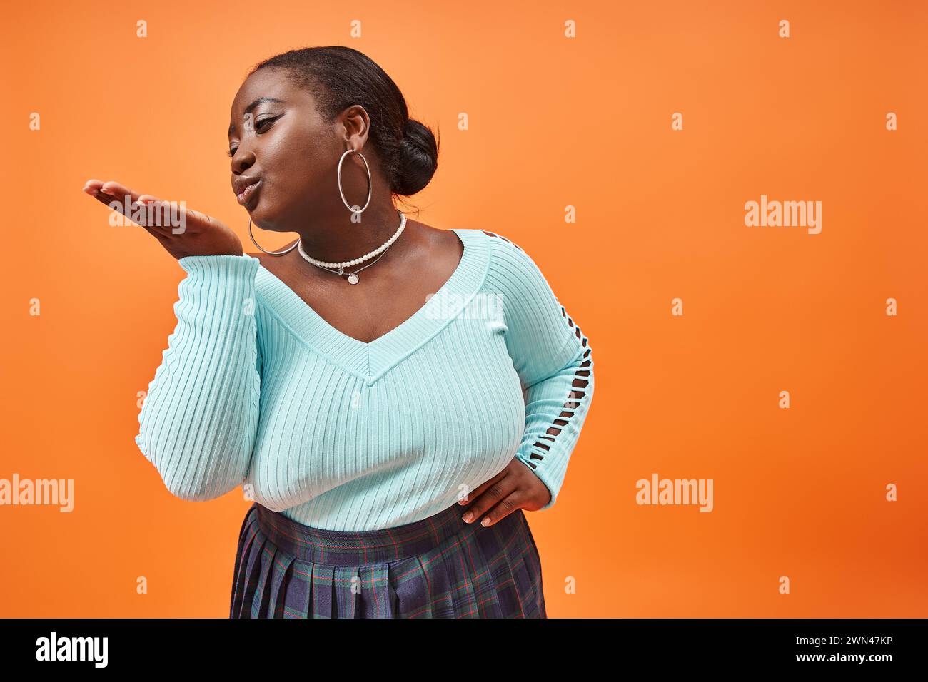 Ludique plus taille afro-américaine femme en jupe à carreaux et manches longues envoyant un baiser d'air Banque D'Images