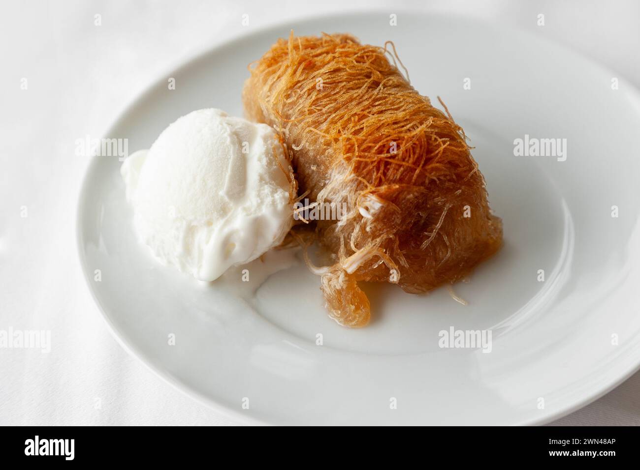 Dessert traditionnel grec kataifi servi avec de la crème glacée sur une assiette blanche. Kataifi grec classique à base de pâte phyllo Banque D'Images