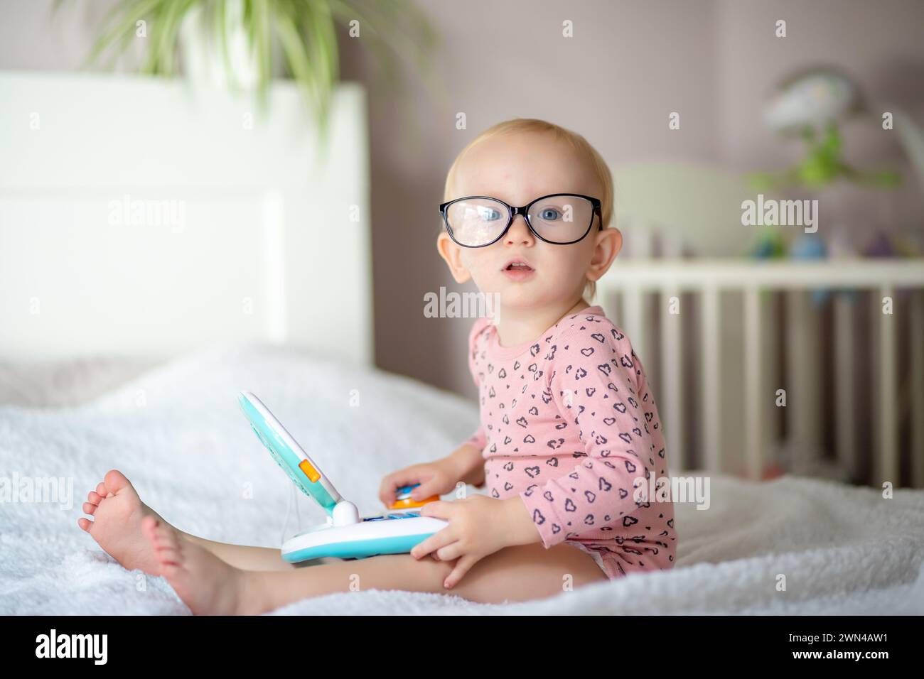Enfant en bas âge avec des lunettes jouant avec un jouet éducatif sur un lit Banque D'Images