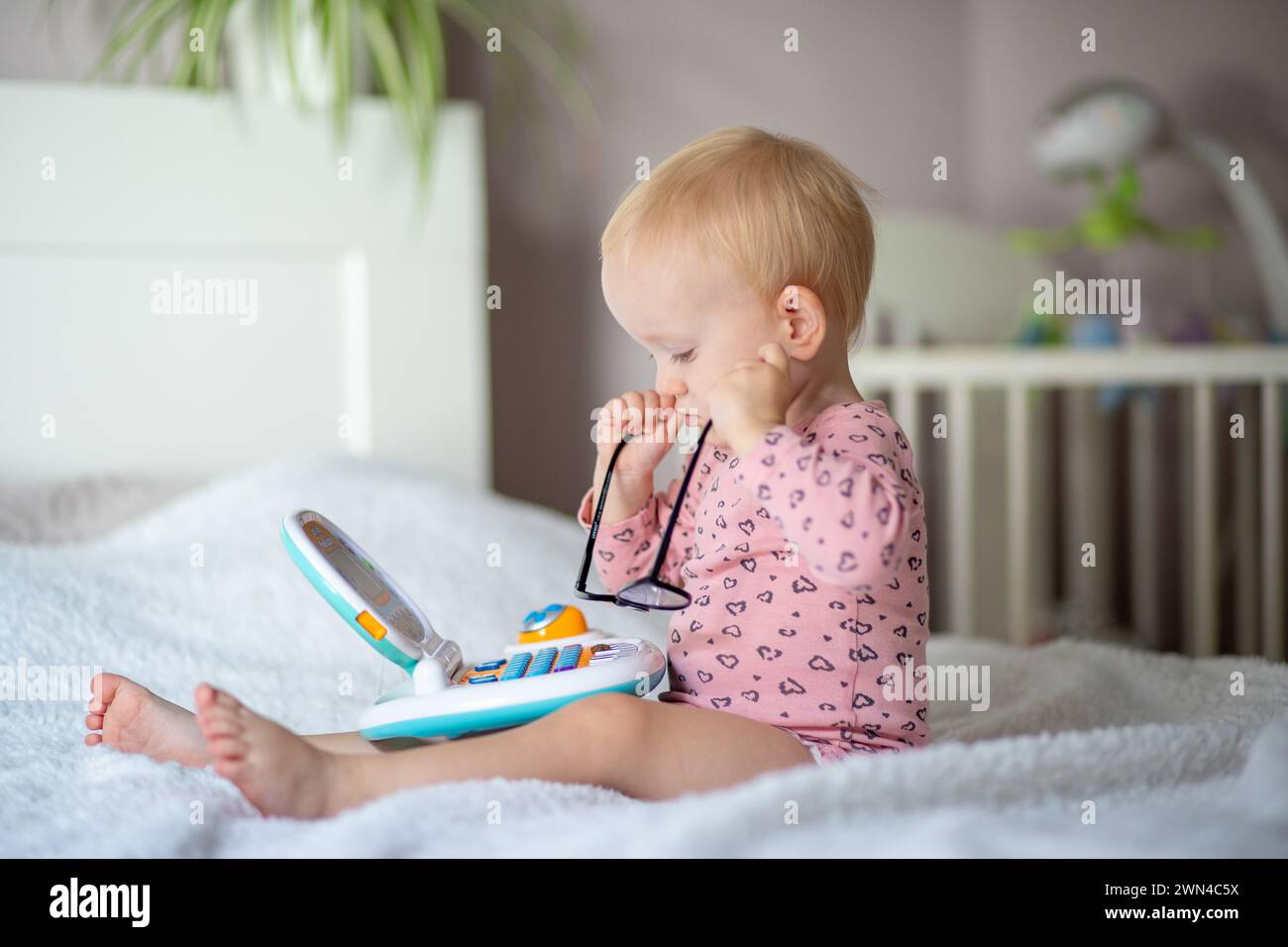 Enfant en bas âge avec des lunettes jouant avec un jouet éducatif sur un lit Banque D'Images
