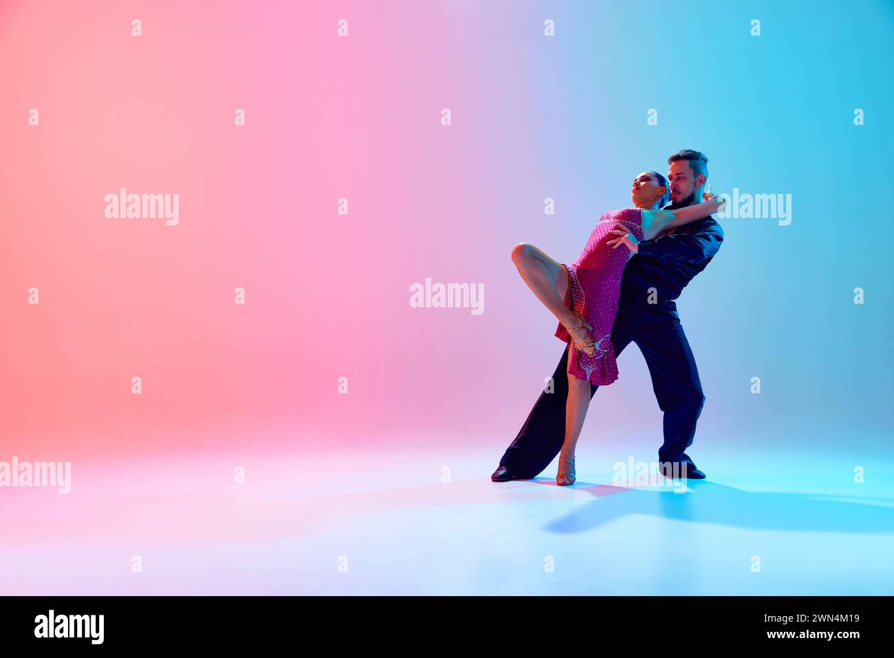Esthétique de la danse. Jeune homme artistique et femme en mouvement, dansant salle de bal sur fond bleu rose dégradé dans la lumière néon Banque D'Images