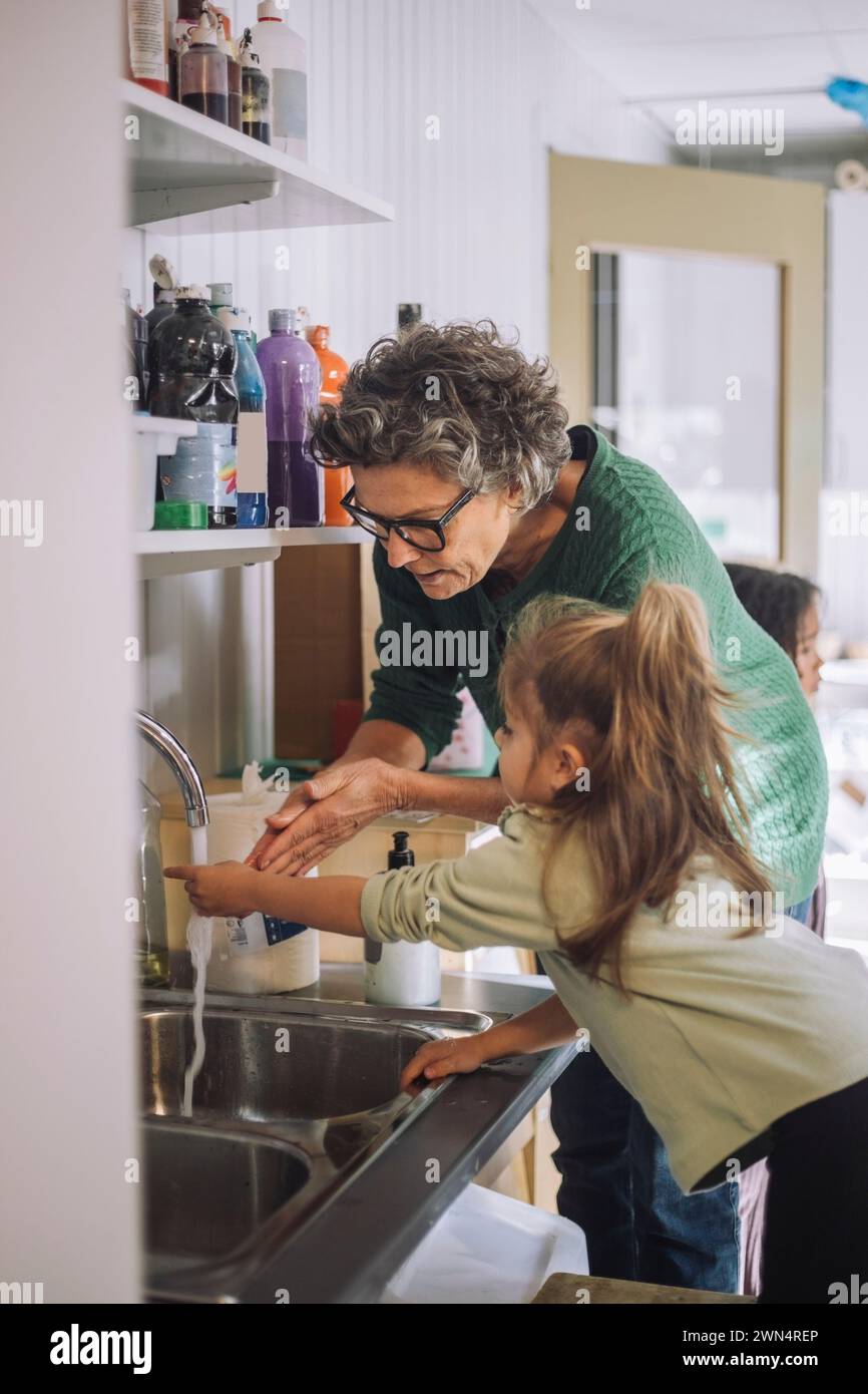 Fille apprenant à se laver les mains avec une enseignante senior à la maternelle Banque D'Images