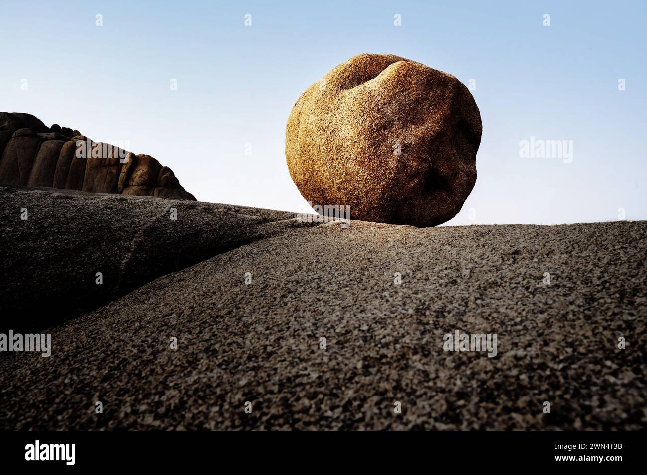 Une boule de rocher presque ronde est illuminée par le soleil doré sur un plateau contre un ciel bleu. Banque D'Images