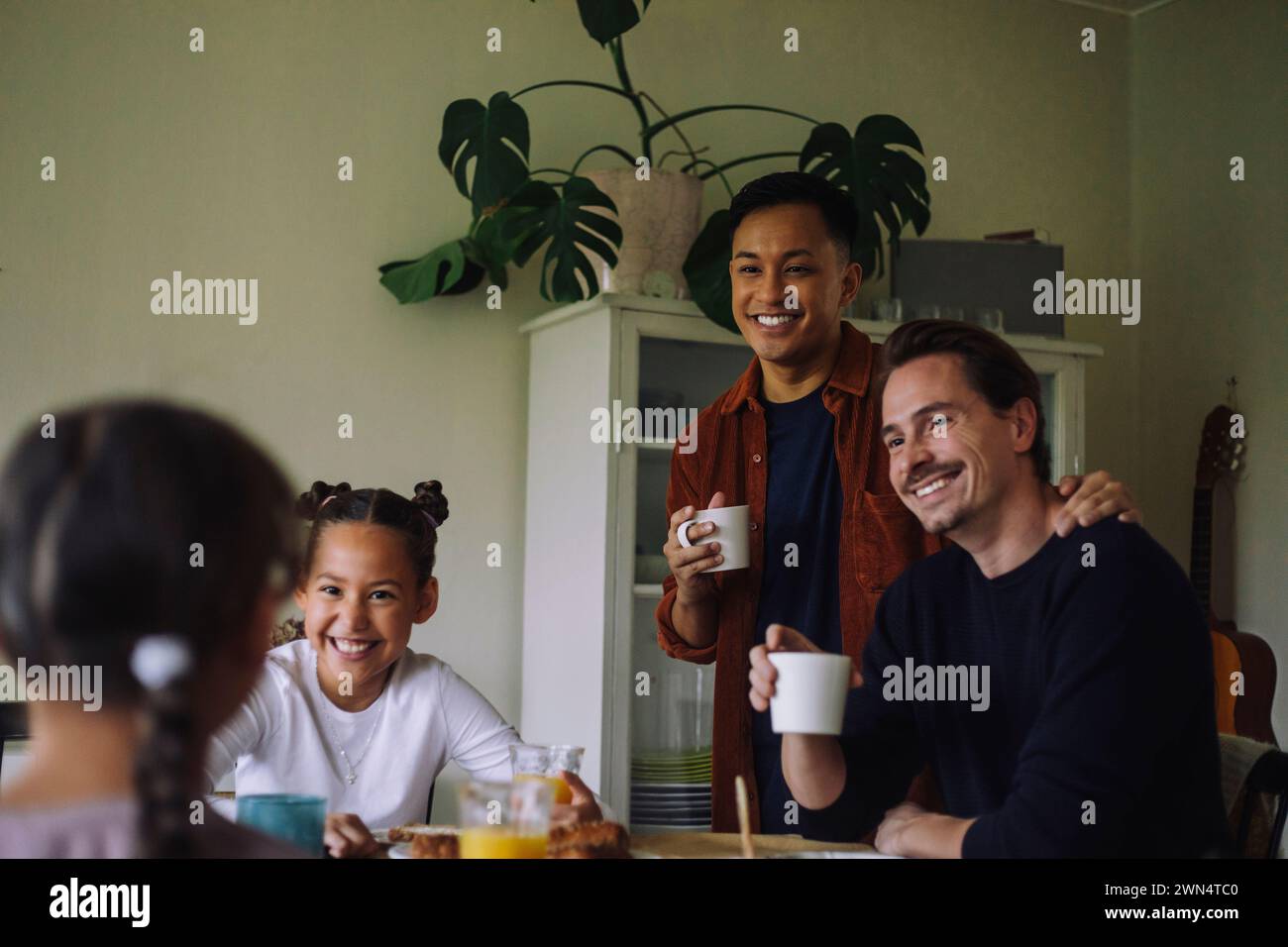 Heureux couple gay parlant avec des filles tout en prenant le petit déjeuner à la maison Banque D'Images