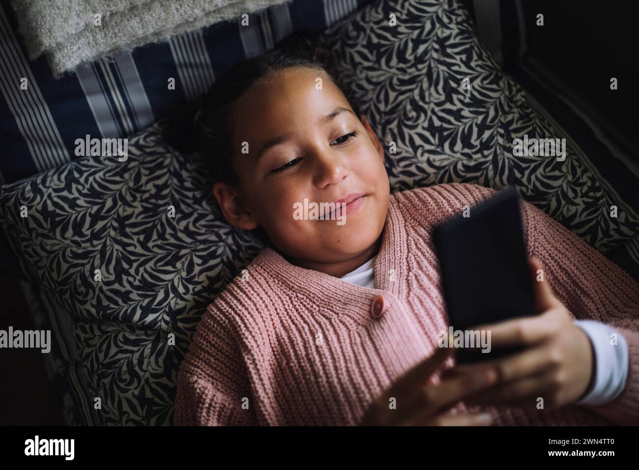 Vue à angle élevé de la fille souriante à l'aide d'un téléphone intelligent tout en étant allongé sur le lit à la maison Banque D'Images