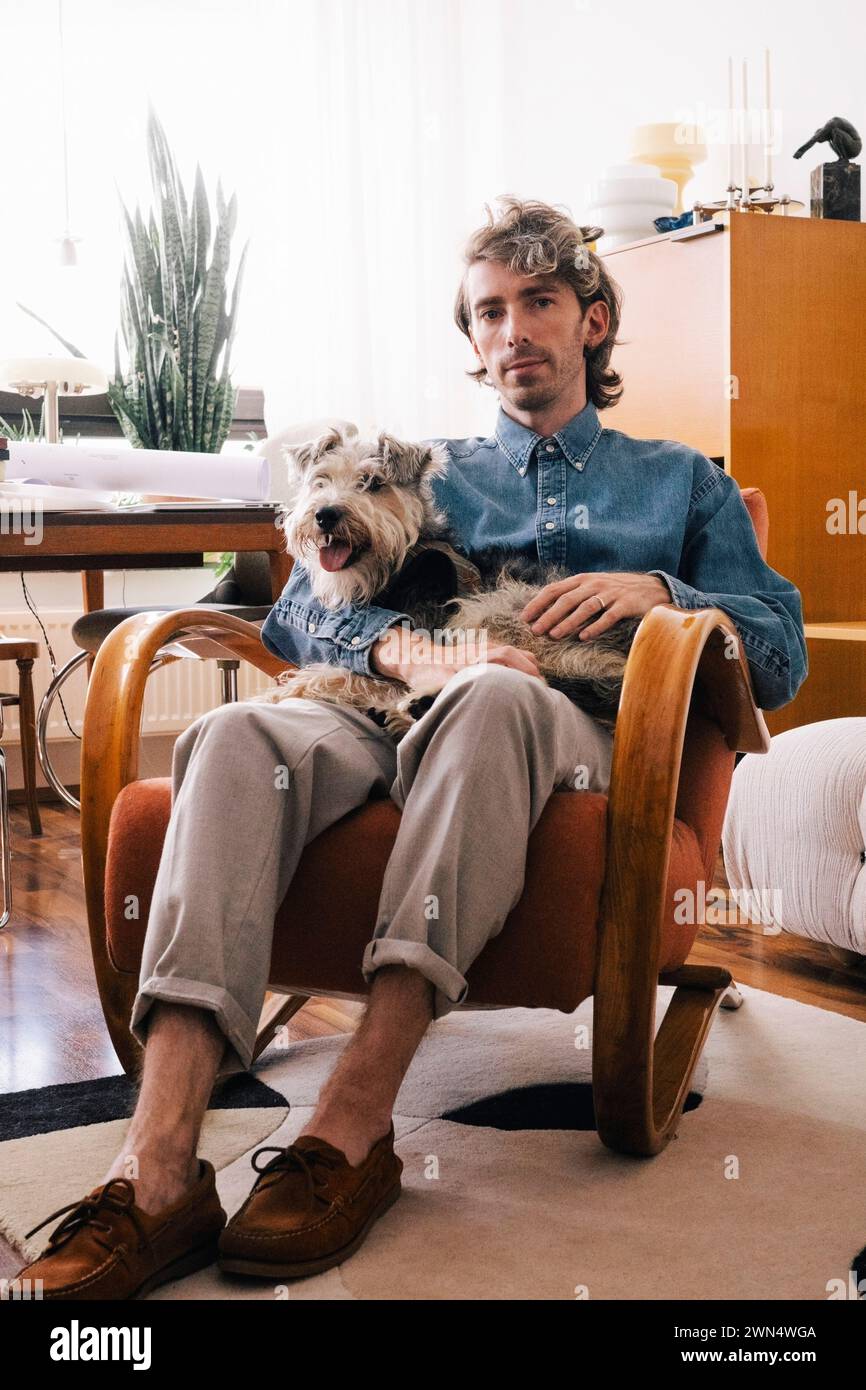 Portrait d'architecte masculin portant chien assis sur un fauteuil au bureau à domicile Banque D'Images