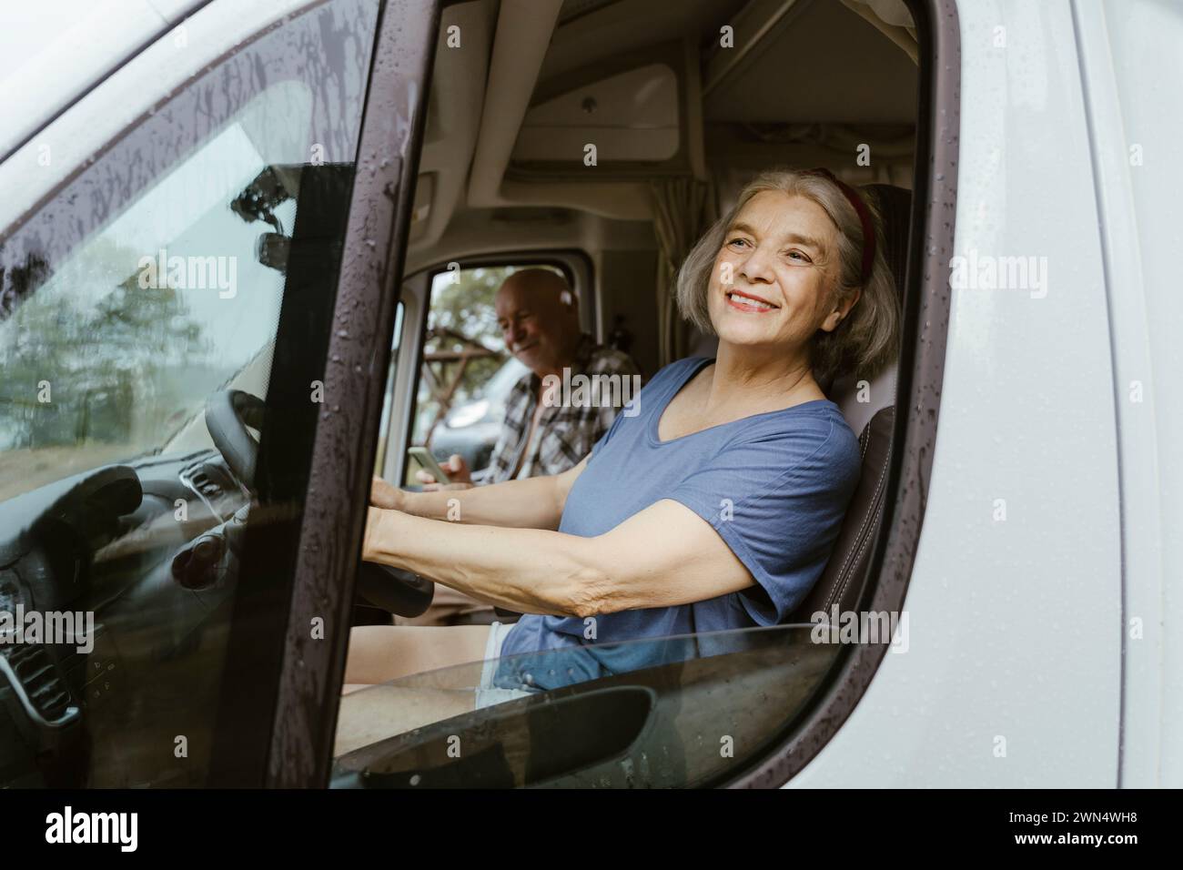 Femme âgée souriante conduisant le camping-car avec l'homme pendant le voyage sur la route Banque D'Images