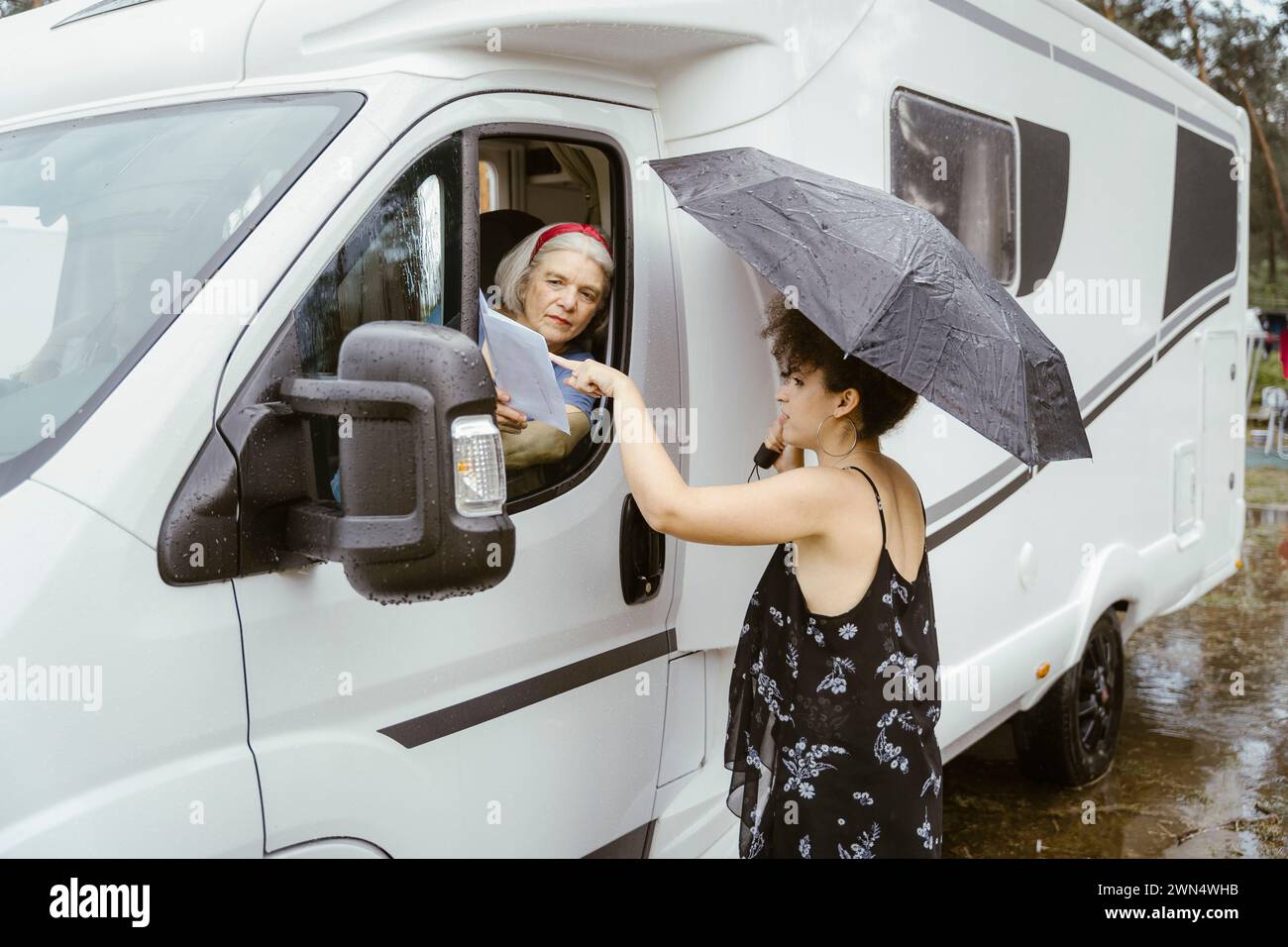 Jeune femme avec parapluie aidant la femme senior pour la direction Banque D'Images