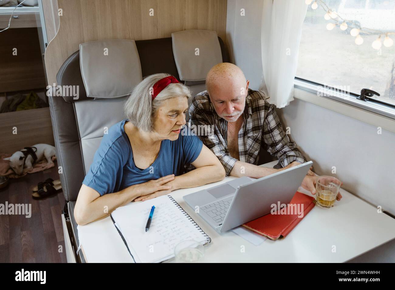 Curieux couple senior assis avec ordinateur portable à table dans le camping-car Banque D'Images