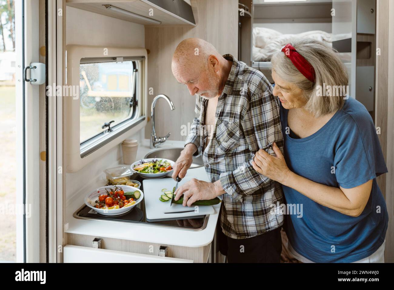 Femme senior debout derrière l'homme coupant le concombre dans le camping-car Banque D'Images