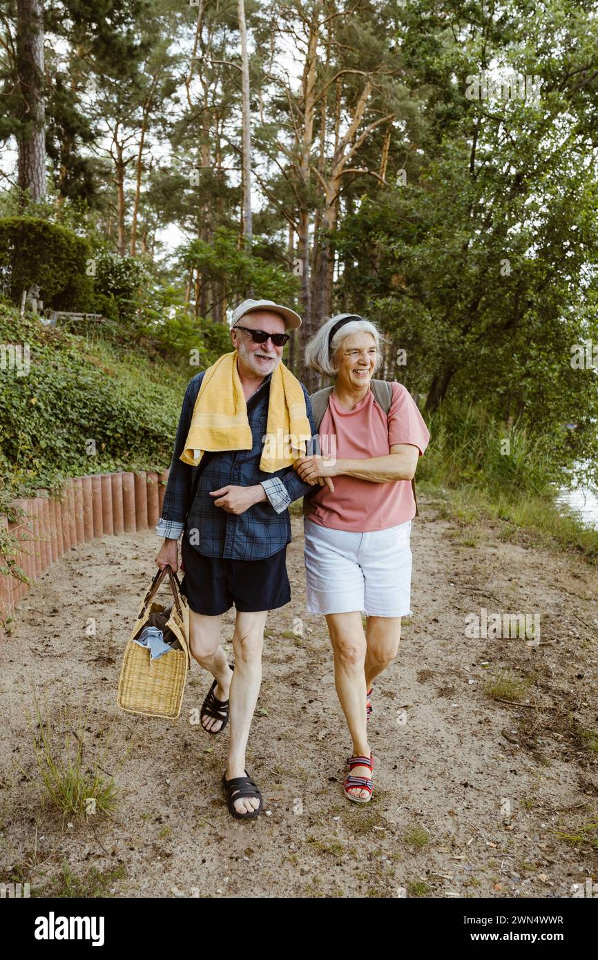 Pleine longueur de couple de personnes âgées retraitées souriantes marchant ensemble tout en faisant de la randonnée dans la forêt Banque D'Images