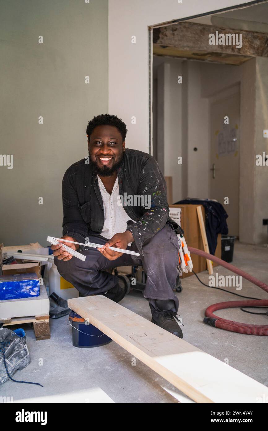 Portrait de charpentier joyeux avec instrument de mesure et planche dans l'appartement Banque D'Images