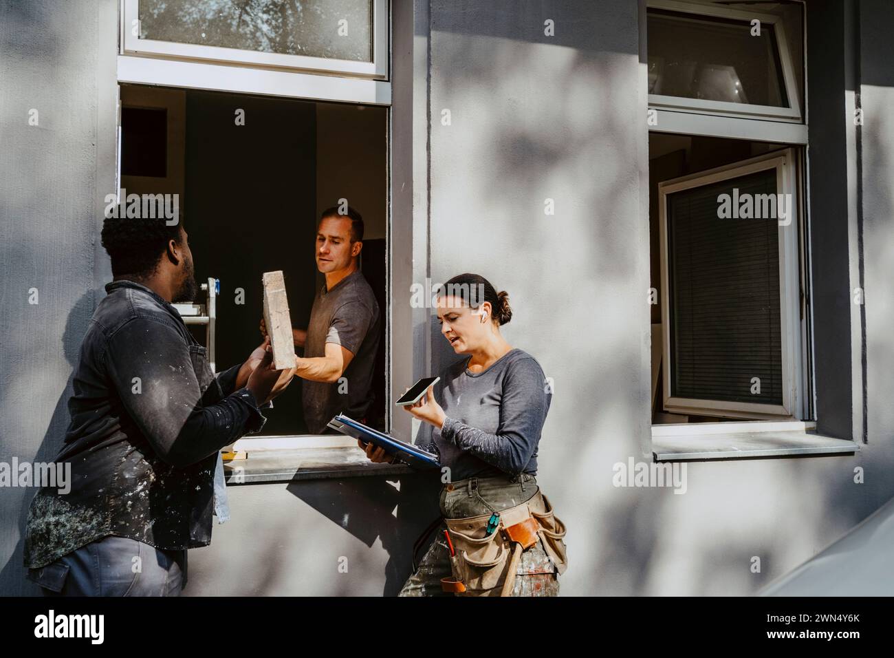 Les ouvriers passent la planche à travers la fenêtre tandis que le directeur de construction féminin parle au téléphone à l'extérieur de la maison Banque D'Images