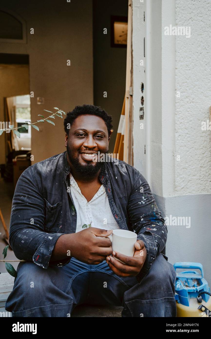 Portrait de charpentier masculin souriant tenant avoir le café à la porte de la maison Banque D'Images