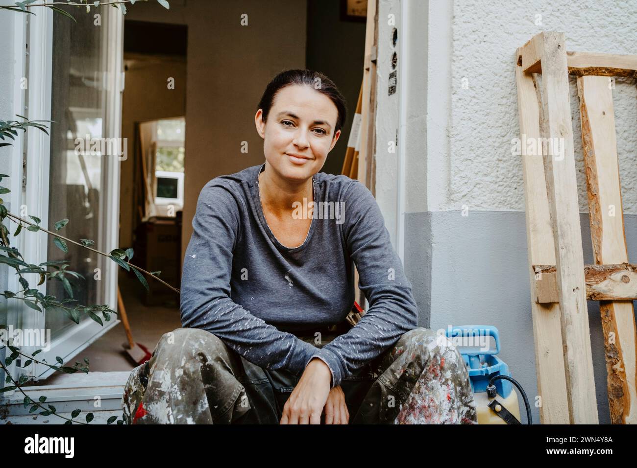Portrait de charpentier féminin souriant assis devant l'entrée de la maison Banque D'Images