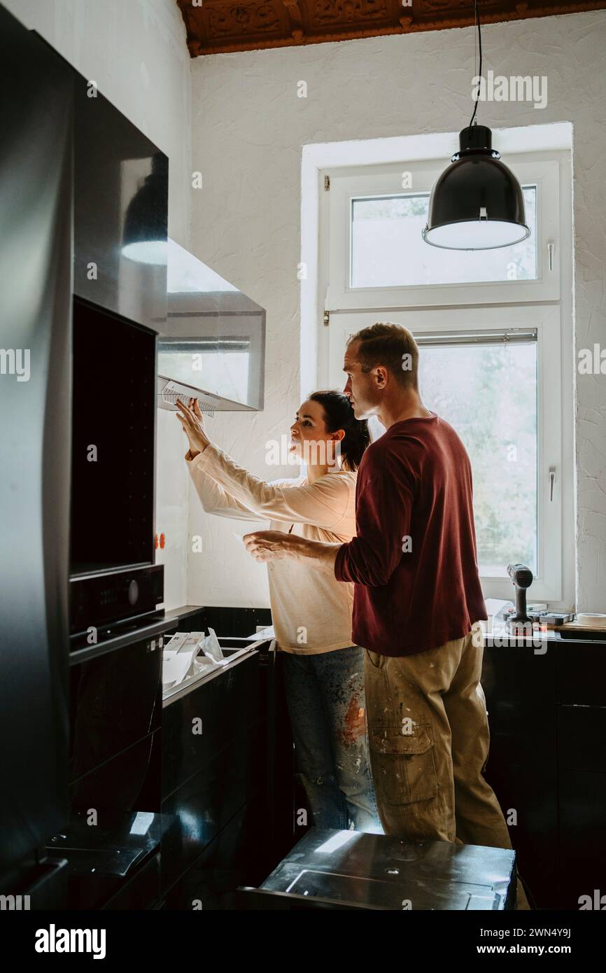 Vue latérale de couple fixant l'armoire dans la cuisine lors de la rénovation de la maison Banque D'Images