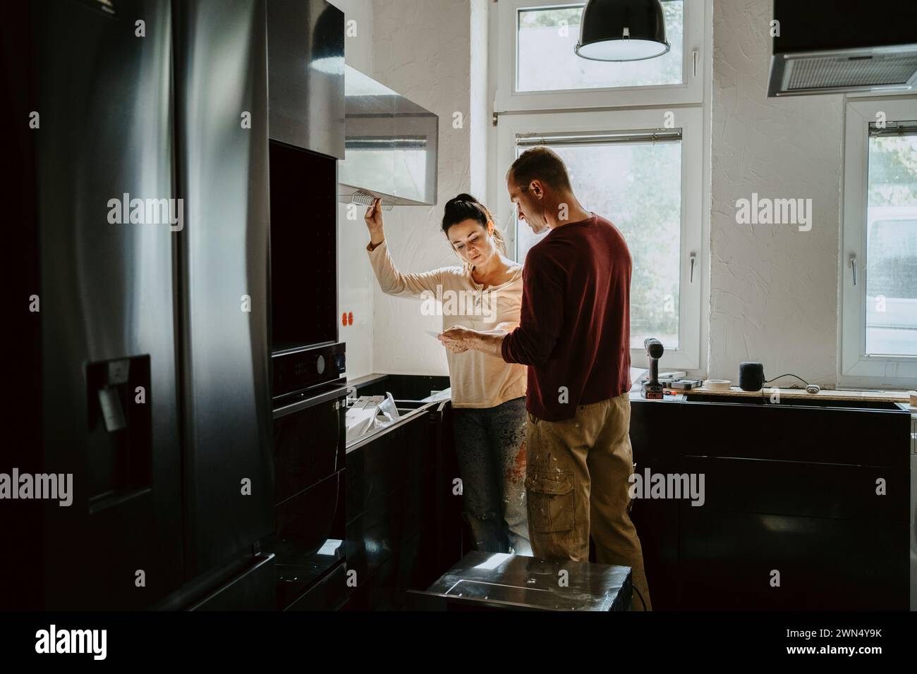 Couple discutant tout en fixant l'armoire dans la cuisine lors de la rénovation de la maison Banque D'Images