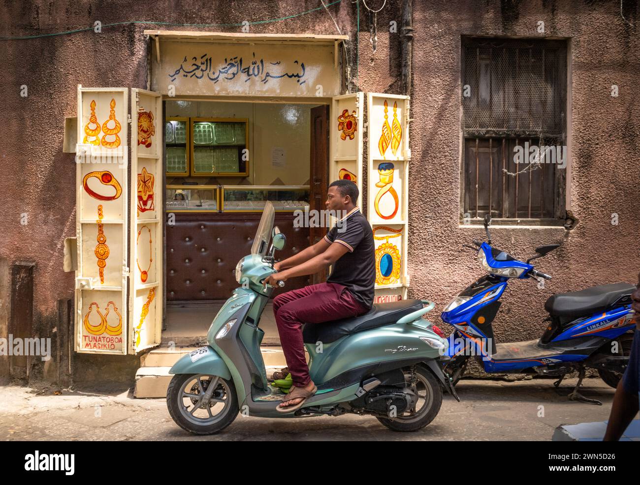 Un homme sur un scooter passe devant une bijouterie à Stone Town, Zanzibar, Tanzanie Banque D'Images