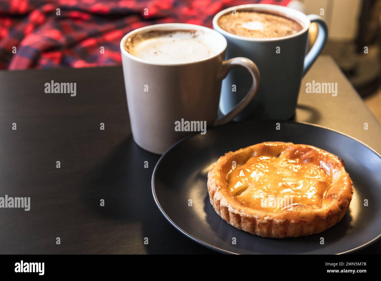 Pastel de nata, pâtisserie portugaise à la crème anglaise aux œufs est sur la table noire avec deux tasses de cappuccino Banque D'Images