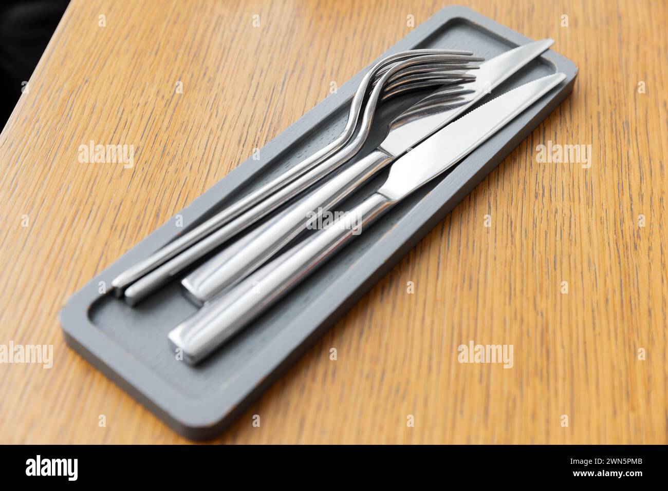 Fourchettes et couteaux brillants en acier inoxydable reposent sur un petit plateau en bois gris sur une table en bois vide Banque D'Images