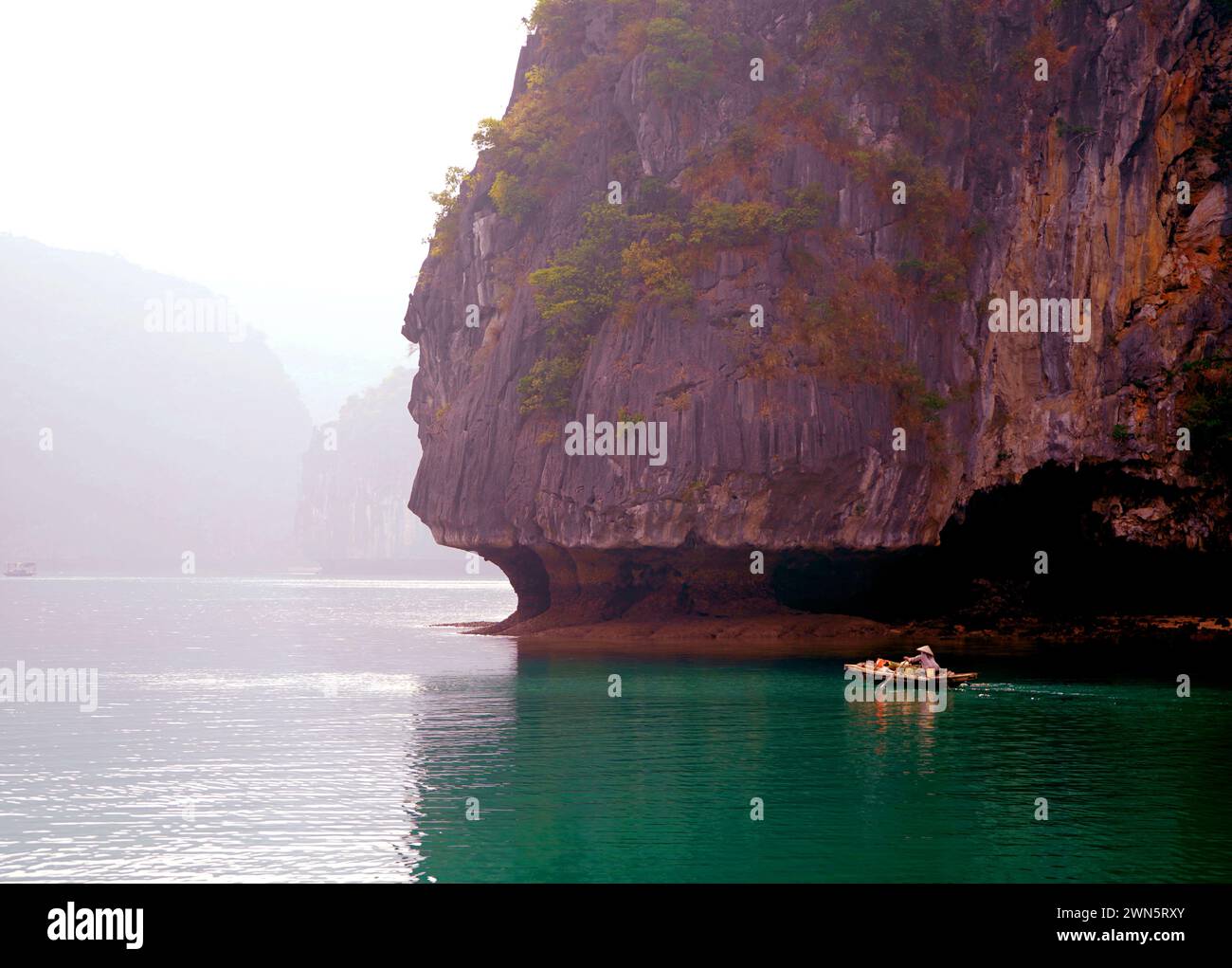 Petit bateau avec fond de falaises calcaires de la baie d'Halong Banque D'Images