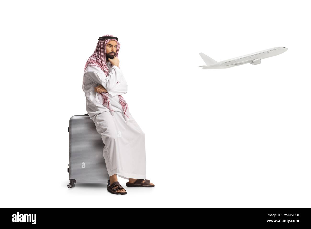 Homme arabe saoudien assis sur une valise et attendant un vol isolé sur fond blanc Banque D'Images