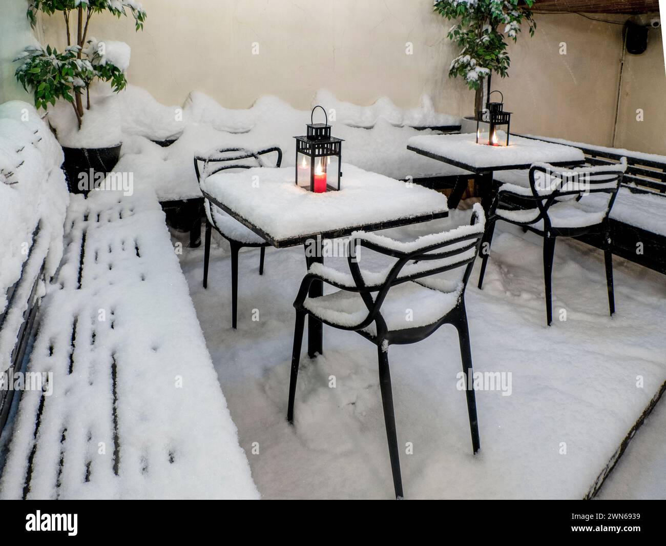 Tables et chaises recouvertes de neige fraîche en hiver, bougie rouge allumée sur la table recouverte de neige fraîche Banque D'Images