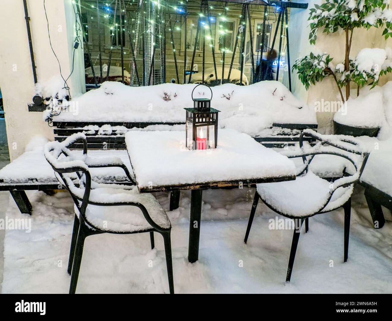 Tables et chaises recouvertes de neige fraîche en hiver, bougie rouge allumée sur la table recouverte de neige fraîche Banque D'Images