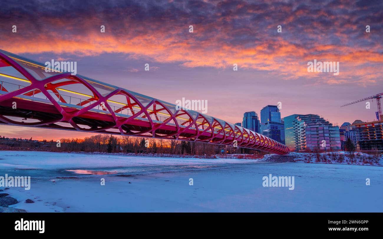Lever de soleil doré au centre-ville de Calgary avec le pont Peace Bridge au-dessus de la rivière Bow gelée et enneigée en hiver. Banque D'Images
