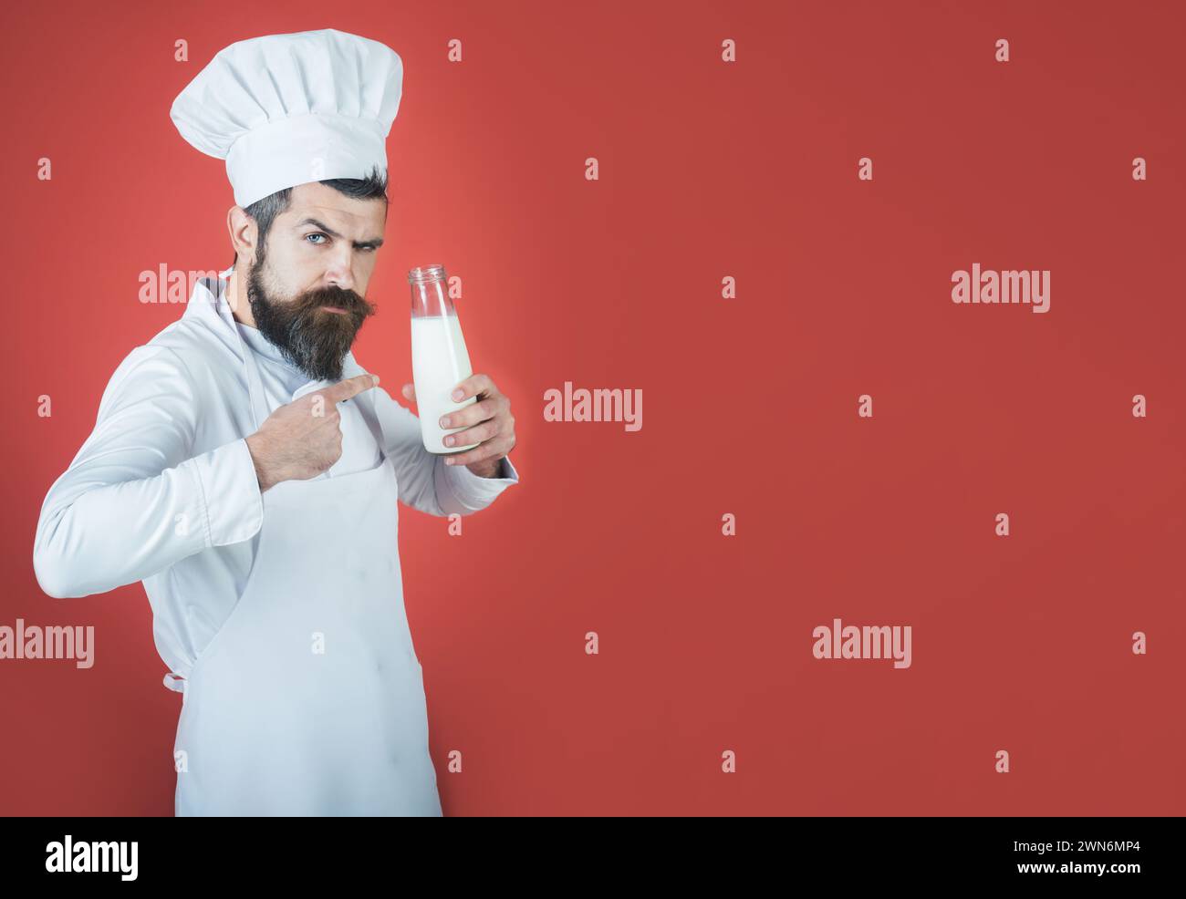 Homme de chef sérieux en uniforme blanc pointant le doigt à la bouteille de boisson de lait. Mâle cuisiner dans un tablier avec une bouteille de kéfir ou de yogourt. Produits laitiers Banque D'Images