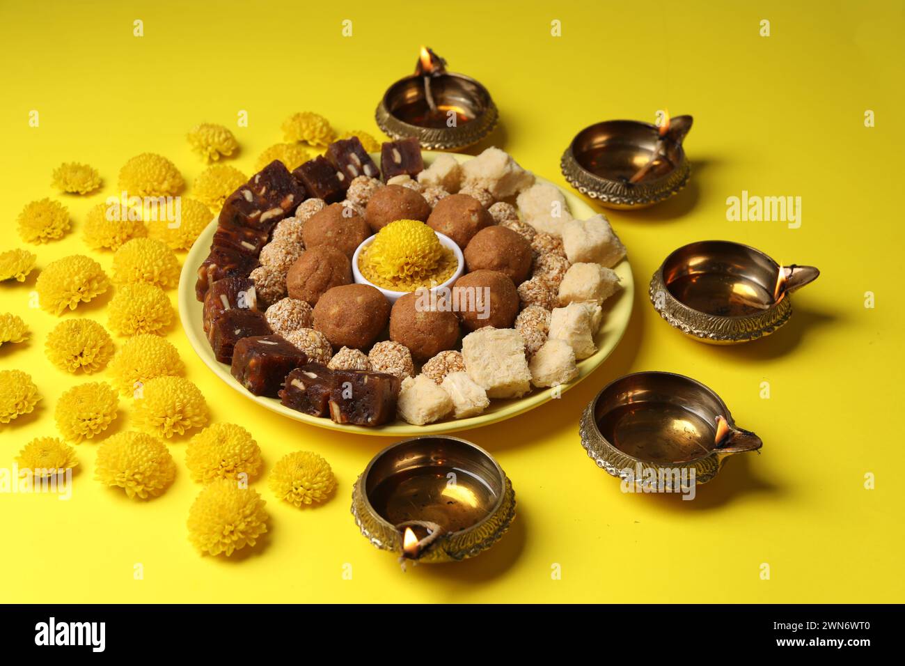 Joyeux Diwali. Composition avec des lampes diya, des fleurs de chrysanthème et de délicieux bonbons indiens sur table jaune Banque D'Images