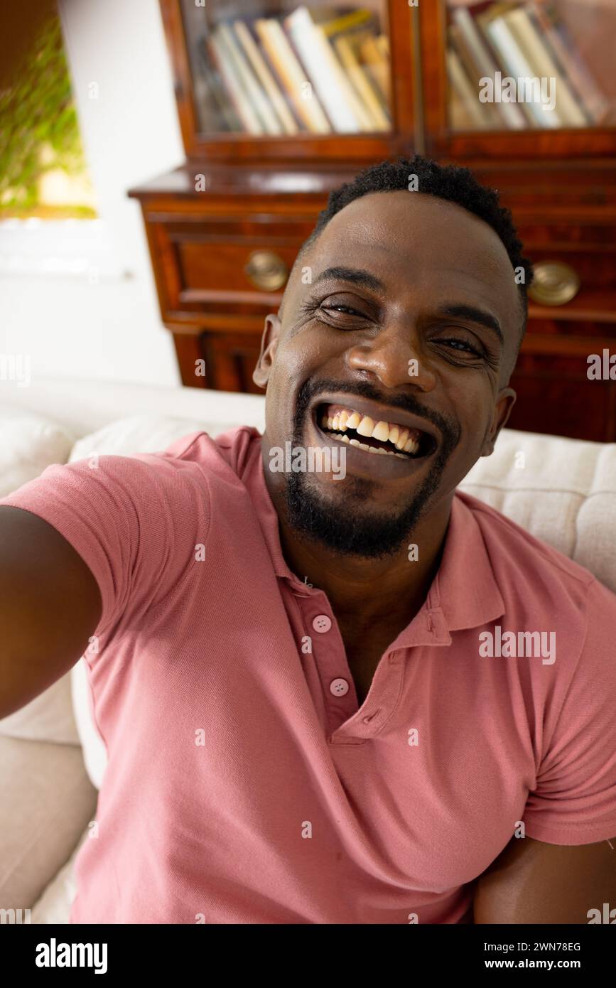 Homme afro-américain avec un sourire éclatant, portant une chemise rose, prenant un selfie Banque D'Images