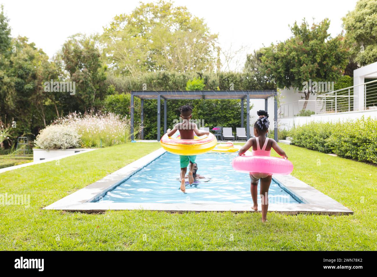 Frères et sœurs noirs avec flotteurs prêts pour le plaisir de la piscine dans une cour luxuriante. Banque D'Images