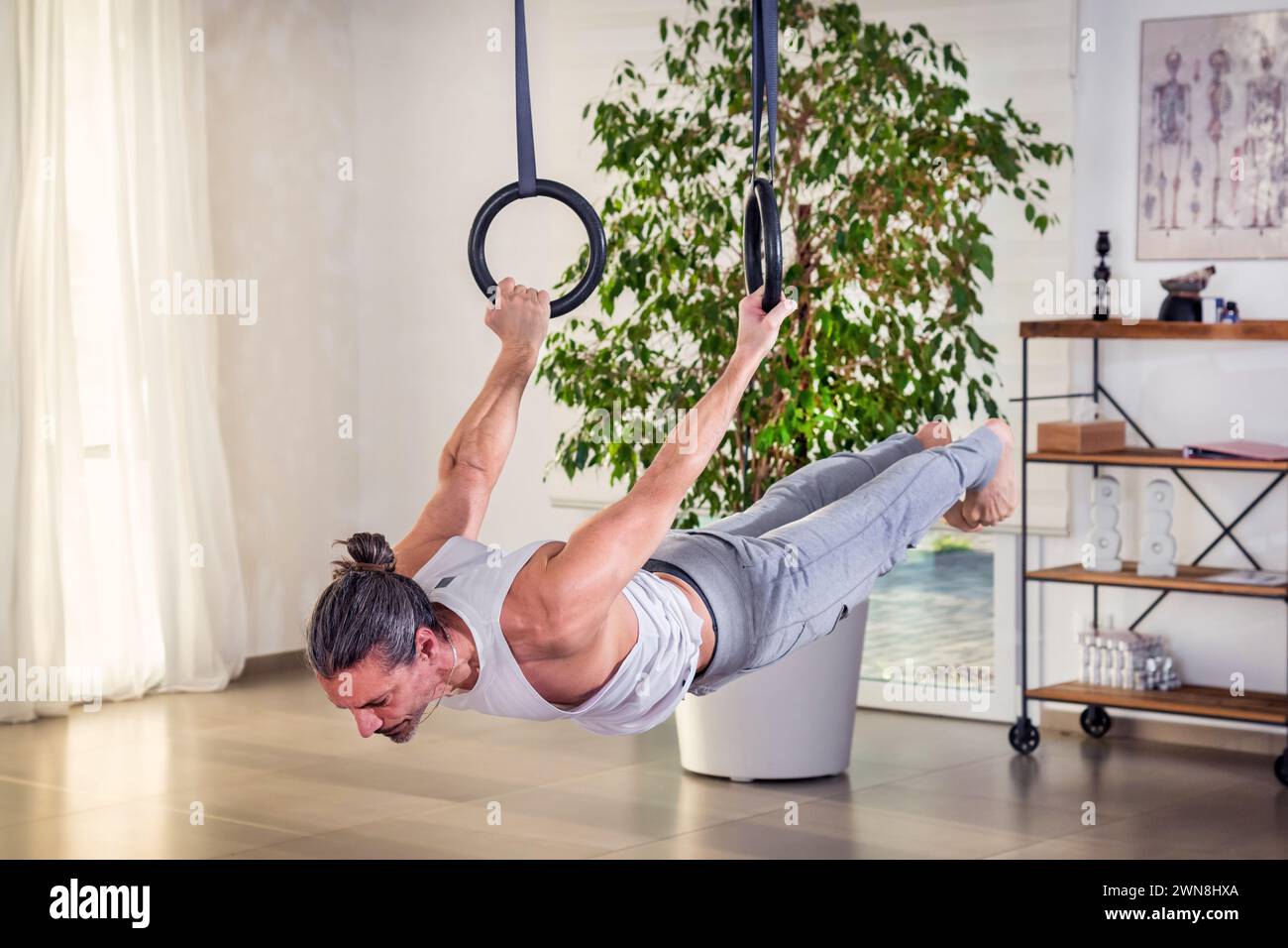 Homme adulte flexible focalisé faisant un exercice d'anneau de levier arrière pendant l'entraînement de fitness à la maison Banque D'Images