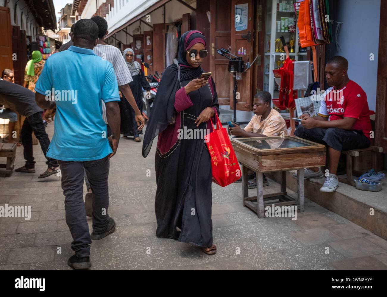 Une femme musulmane portant un buibui traditionnel et un châle de khimar regarde son smartphone au Stone Town Market, Zanzibar, en Tanzanie Banque D'Images