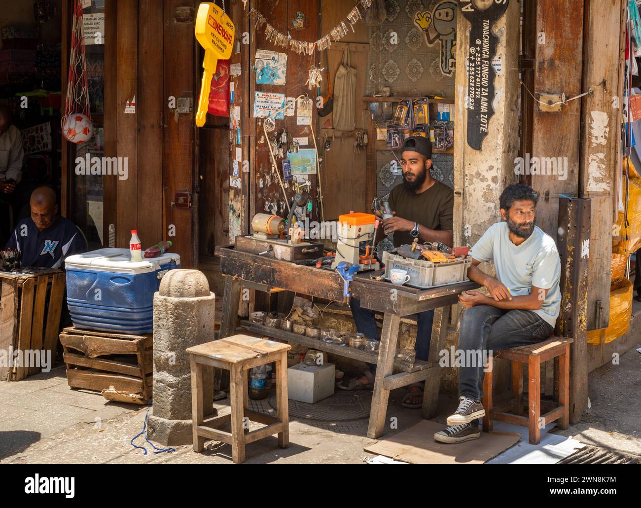 Les hommes sont assis dans un atelier de découpe de clés à Stone Town Market, Zanzibar, Tanzanie Banque D'Images