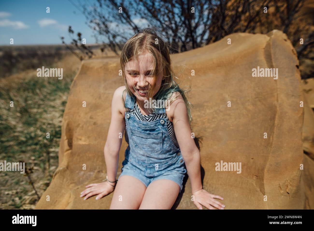 Preteen Girl sourit tout en étant assis sur le rocher dans la scène de la nature. Banque D'Images