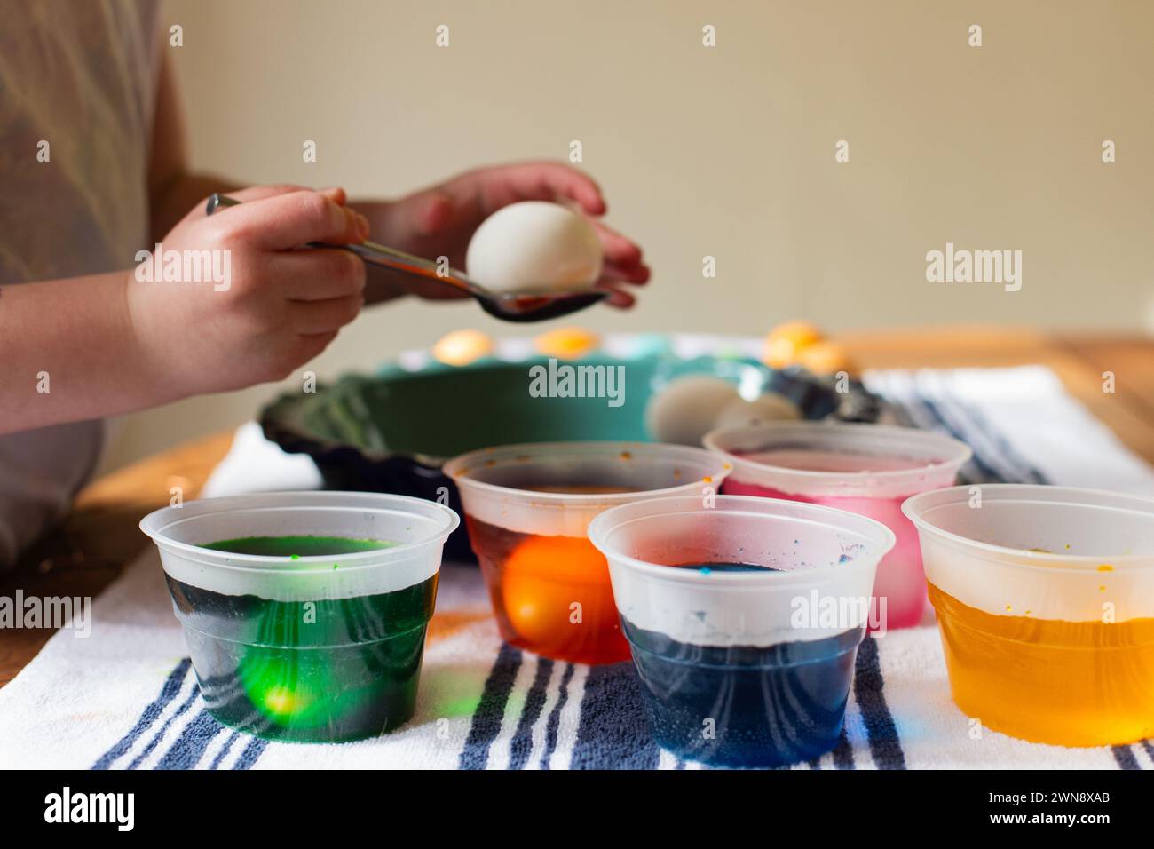 Mains d'enfant coloriant les oeufs de Pâques dans des gobelets en plastique Banque D'Images