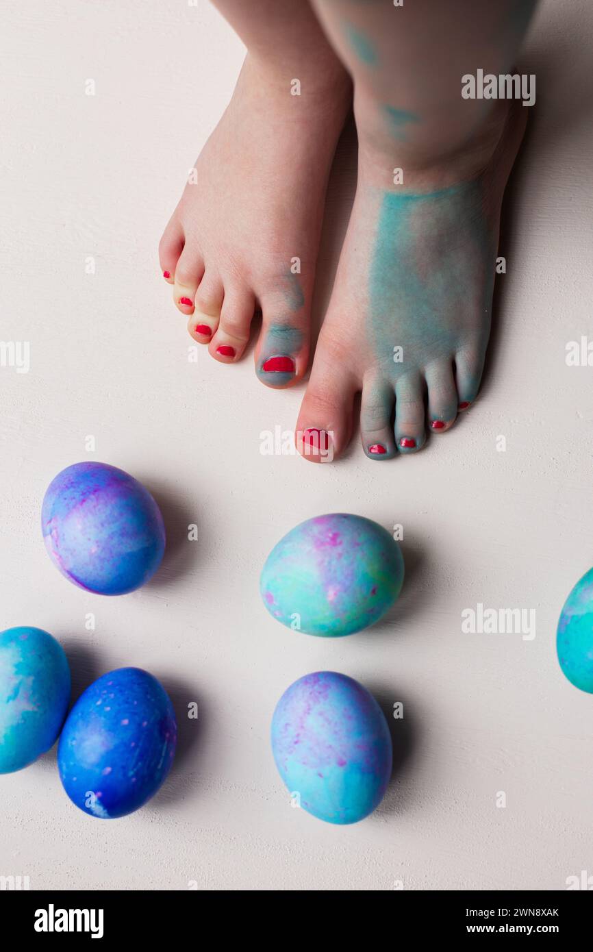 Pieds d'enfant debout près d'oeufs de Pâques teints en bleu Banque D'Images